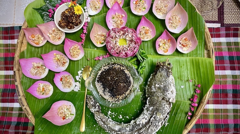 Isaan Thai food fish with pink lotus flower leaf and herbs with exquiste presentation on banana leaf and bamboo tray